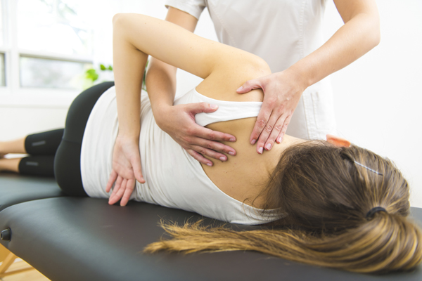 Een vrouw ligt op haar rechterzij met een hand op haar rug tijdens een behandeling van een chiropractor.